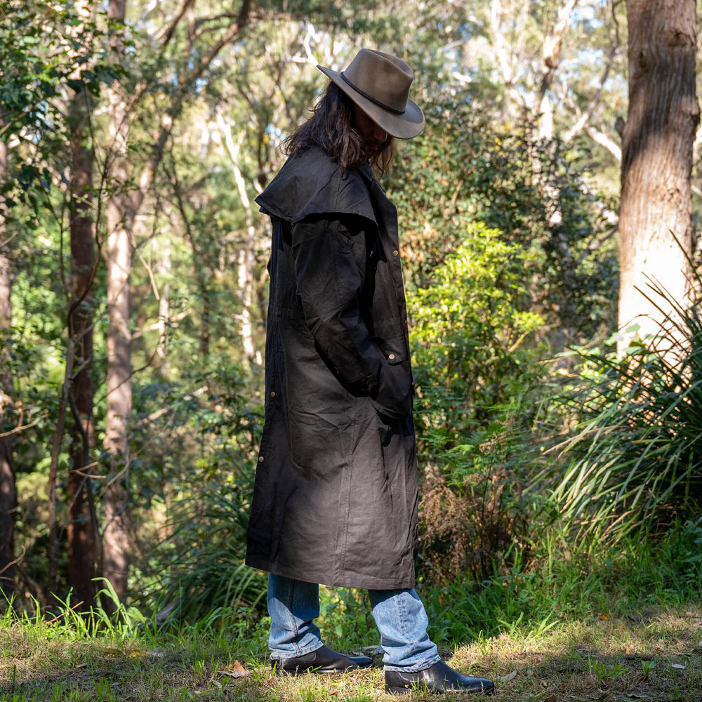 Person wearing a long dark coat and hat in a forest setting